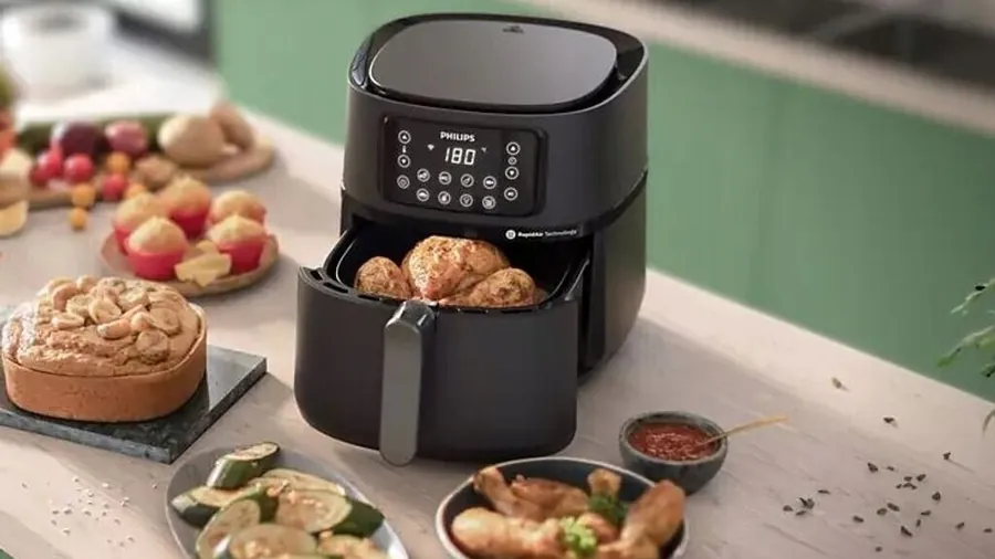 Air fryer Philips à double panier ouvert contenant des pommes de terre et des viandes, entouré de plats préparés