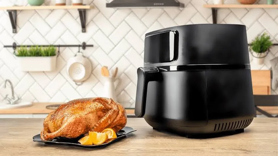 Air fryer noir posé près d'un poulet rôti entier sur un plat, dans une cuisine claire à carrelage métro