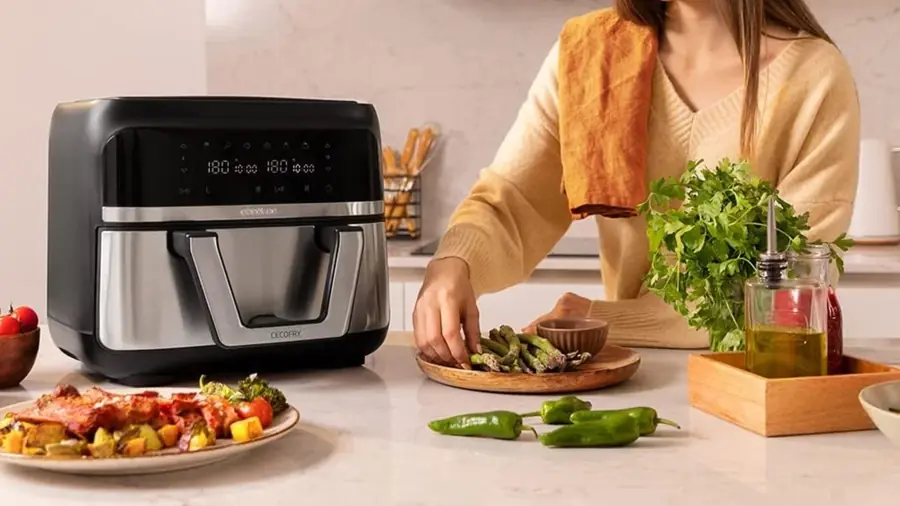 Air fryer posé sur un plan de travail pendant qu'une personne prépare des légumes verts